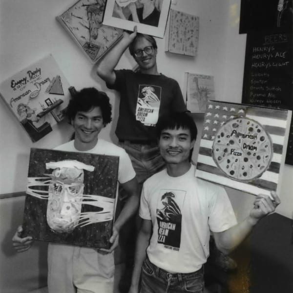 Three men in American Dream Pizza shirts proudly display their pizza-themed artwork.
