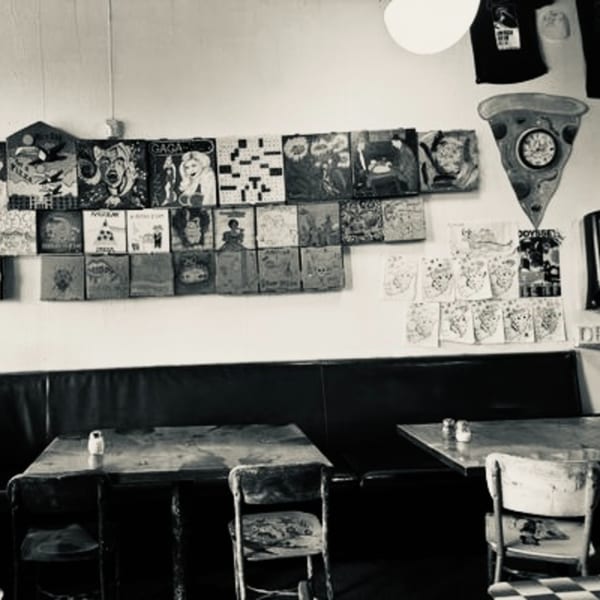 Black and white photo of a restaurant interior with tables, chairs, and eclectic art on the wall.