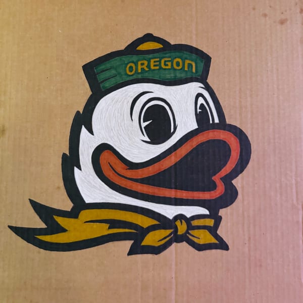 The Oregon Ducks mascot, a cartoon duck head with a green hat and yellow bow, on cardboard.