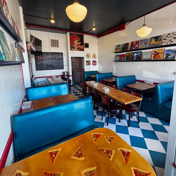 A retro-style pizza restaurant interior with blue booths, checkered floors, and quirky wall art.