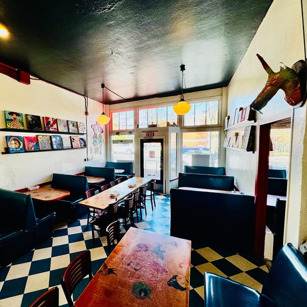 Interior of a restaurant with checkered floors, booths, tables, and artwork on the walls.