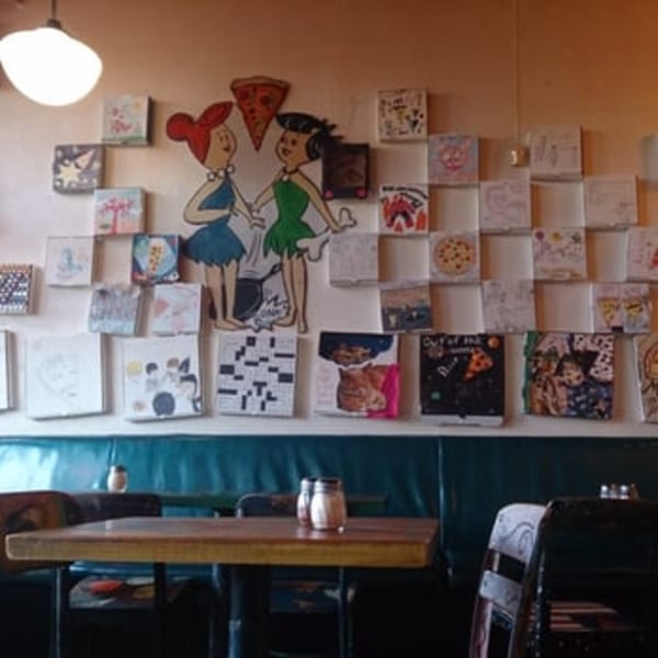 Restaurant interior with Flintstones characters on the wall, surrounded by small framed art and a table with shakers.