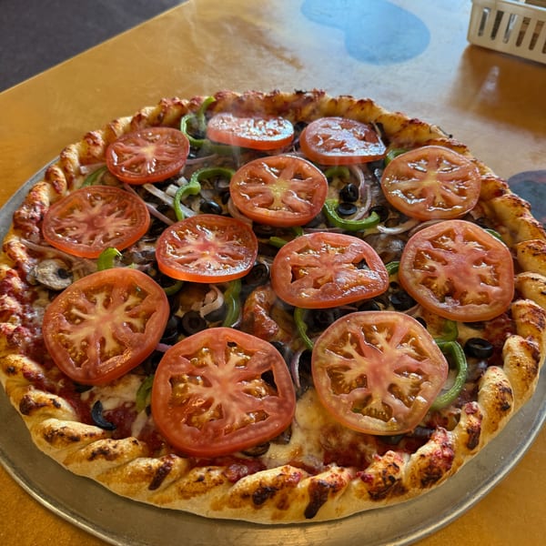 Steaming hot vegetarian pizza with tomatoes, green peppers, onions, mushrooms, and black olives.
