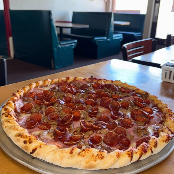 A large, freshly baked pizza with pepperoni, sausage, and ham sits on a table in a restaurant.