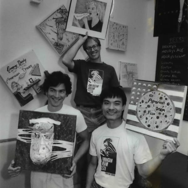 Three men in American Dream Pizza shirts proudly display their pizza-themed artwork.