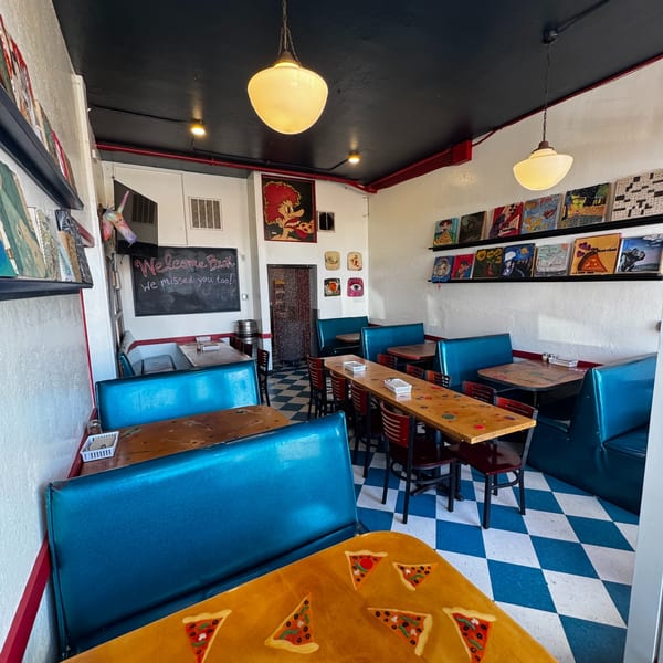 A vibrant restaurant interior with blue booths, wooden tables, checkered floors, and quirky wall art.