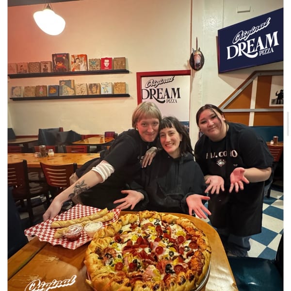 Three smiling women pose with a large pizza and breadsticks at Original Dream Pizza.
